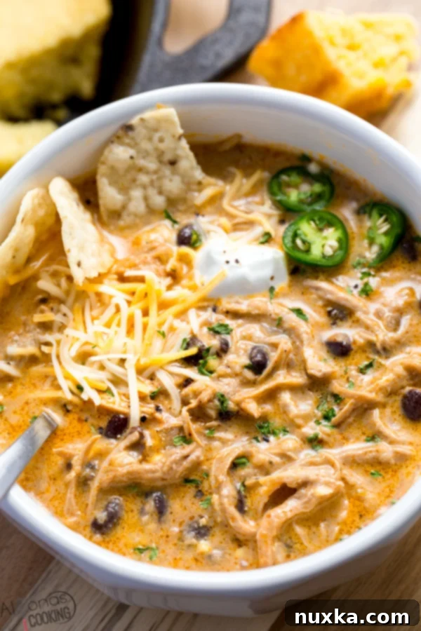 A steaming bowl of creamy Instant Pot White Chicken Chili, garnished with fresh cilantro, sour cream, and a slice of lime, showcasing the rich texture with chicken, beans, and corn visible.
