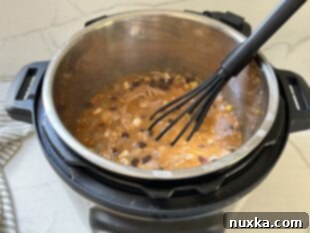 A whisk being used to stir the cooked white chicken chili in the Instant Pot, smoothing out any cream cheese lumps before serving.