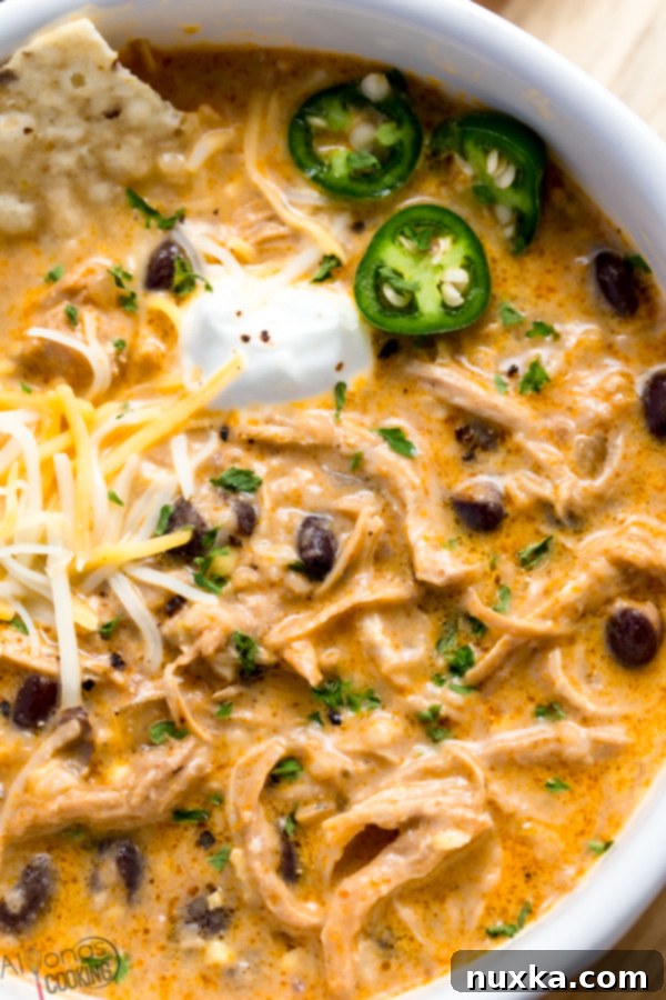 A close-up shot of a creamy white chicken chili with visible shredded chicken, corn kernels, and beans, in an Instant Pot, ready to be served.