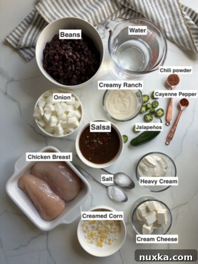 All the essential ingredients for Instant Pot white chicken chili laid out: drained beans, chicken breasts, water or broth, creamy ranch dressing, jalapeños, chili powder, salt, creamed corn, cream cheese, heavy cream, diced onion, and salsa.