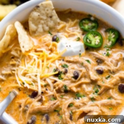 Easy Instant Pot White Chicken Chili 4 A close-up of a bowl of creamy Instant Pot White Chicken Chili, garnished with fresh cilantro, a dollop of sour cream, and a lime wedge.