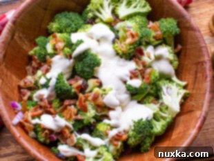 Broccoli salad being tossed in a large bowl with homemade creamy dressing.