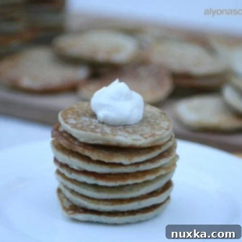 Close-up of golden Ukrainian Potato Pancakes (Deruny) stacked on a white plate, garnished with a dollop of sour cream and fresh herbs.