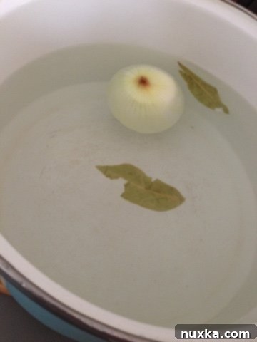 A pot of boiling water with an onion and bay leaves, creating the aromatic broth for Pelmeni soup.