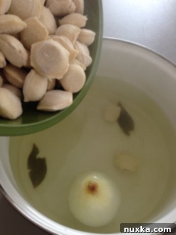 Frozen pelmeni and seasonings being added to the boiling broth with onion and bay leaves.