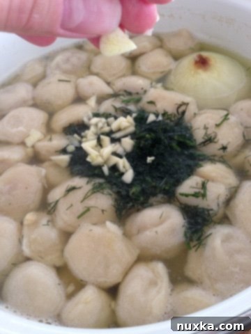 Minced garlic and fresh dill being stirred into the hot Pelmeni soup after cooking.