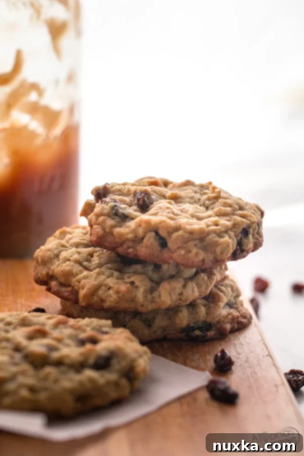 A stack of freshly baked, warm oatmeal raisin cookies with golden edges and soft centers.