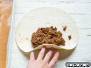 A flour tortilla being filled with ground beef mixture for enchilada assembly.