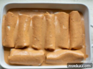 Assembled beef enchiladas in a baking dish, covered with rich red sauce before baking.