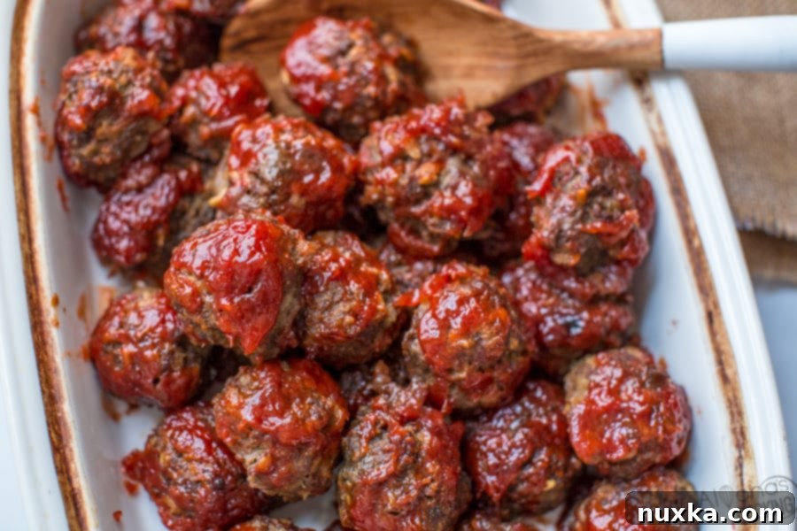 A close-up of baked BBQ meatballs, rich with sauce, in a deep baking dish.