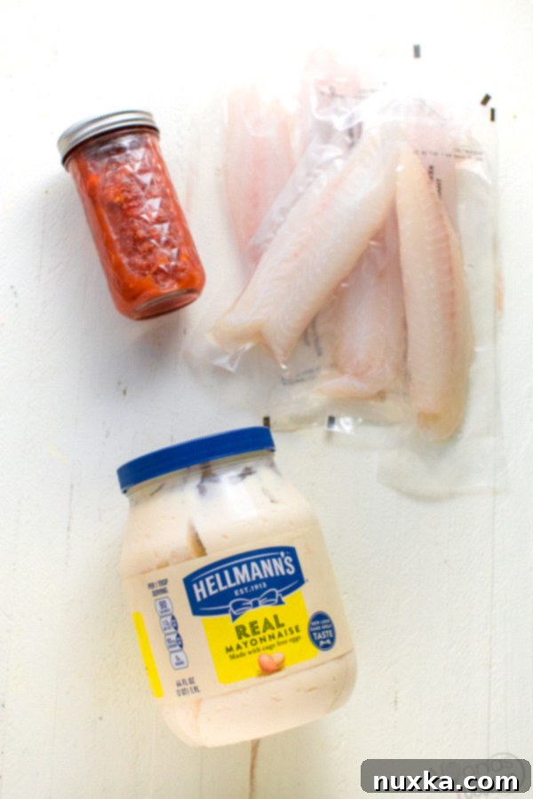 Four raw tilapia fillets seasoned with salt and pepper, laid out on a baking dish, ready for mayonnaise and mango salsa toppings.