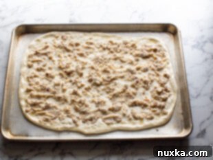 How To Make a Breakfast Pizza: Step one, stretch the pizza dough to a rectangle shape and place into greased sheet-pan. Top with sausage gravy sauce.