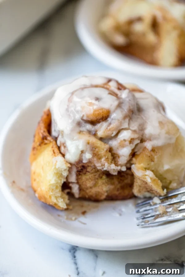 Cinnabon looking cinnamon rolls on a white plate with a fork and a cream cheese frosting, ready to be eaten