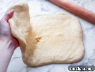 Cinnamon roll dough being folded in half on a work surface