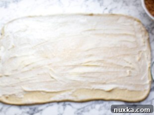 Spreading softened butter over cinnamon roll dough, leaving a border