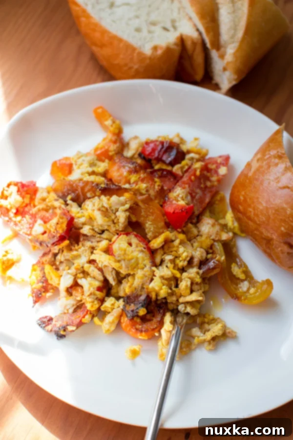 scrambled eggs and seared bell peppers with a side of bread on a plate