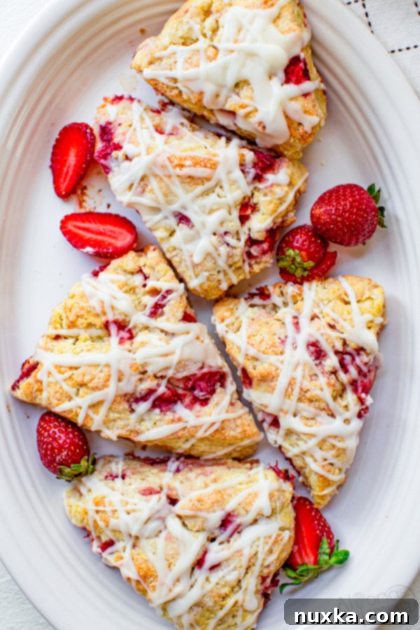 strawberry scones in an oval plate with fresh strawberries and powdered sugar glaze