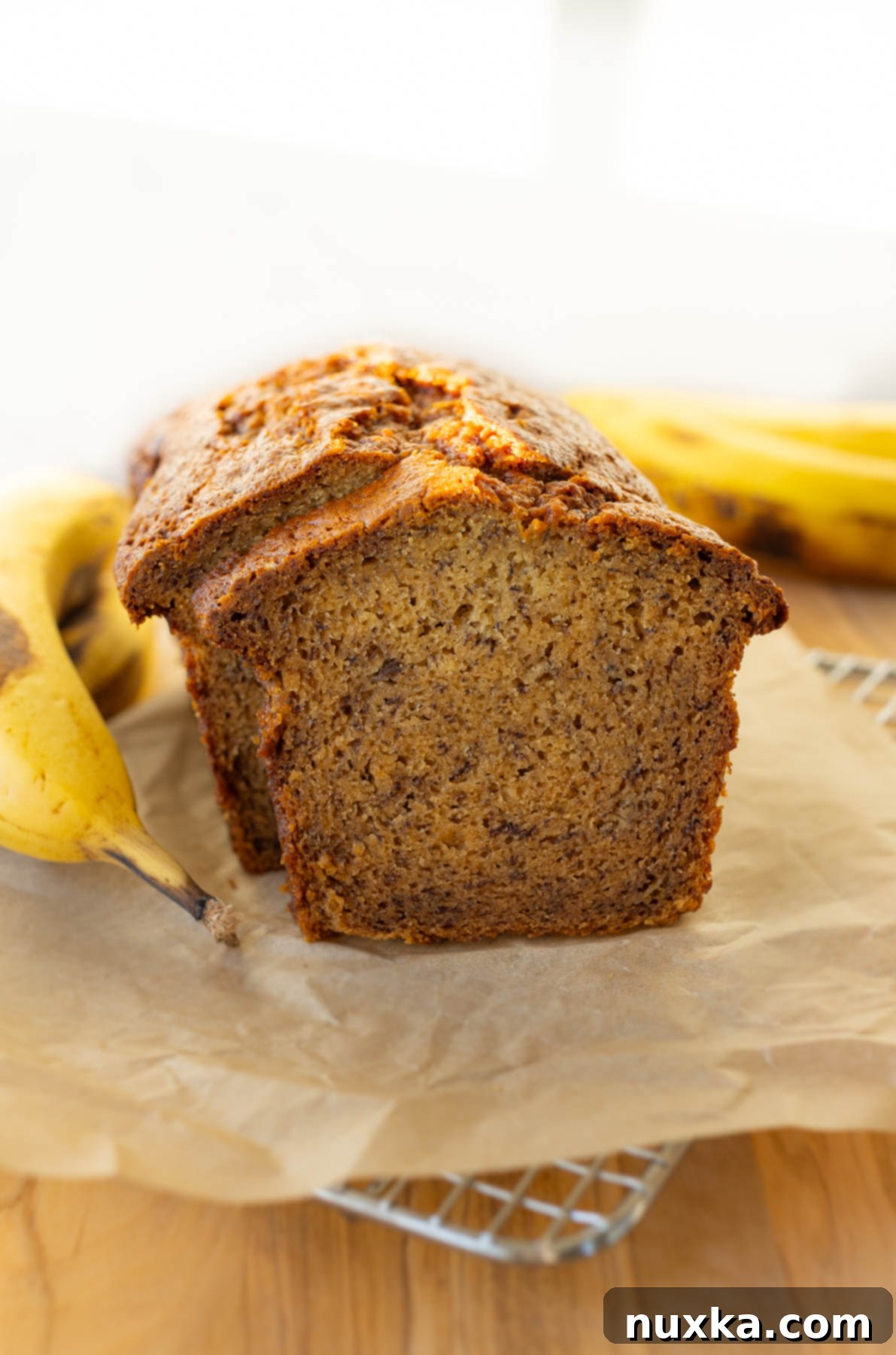 Moist banana bread loaf on a wire cooling rack, lined with parchment paper, allowing it to cool completely after baking.