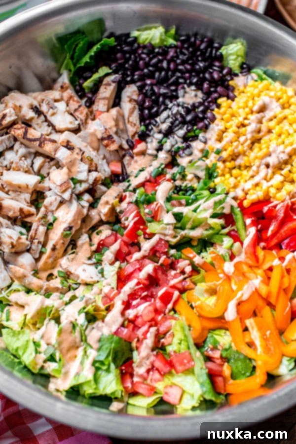 southwest salad in a large mixing bowl with black beans, corn, grilled chicken, bell peppers, tomatoes, chipotle ranch dressing, and romaine lettuce