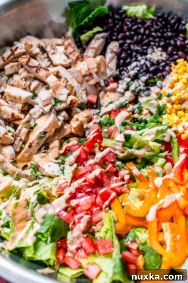 southwest chicken salad in a mixing bowl with grilled chicken, black beans, corn, tomatoes, bell peppers, romaine lettuce and a creamy chipotle ranch dressing 
