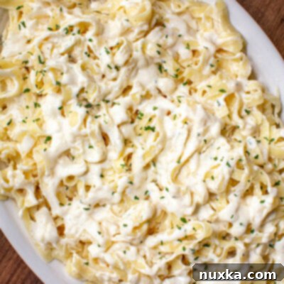 super creamy and rich fettuccine Alfredo sauce smothered in fettuccine pasta and parsley flakes on a white serving dish with a fork