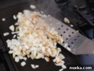 Image of how to cook and sauté onions for a Philly CheeseSteak using a large flat grill spatula
