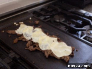 image of provolone cheese melting on top of cooked beef shavings on a hot griddle for Philly Cheesesteaks