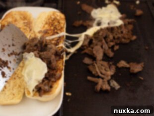 image of Philly Cheesesteak filling being scooped inside a footlong bread roll with provolone cheese