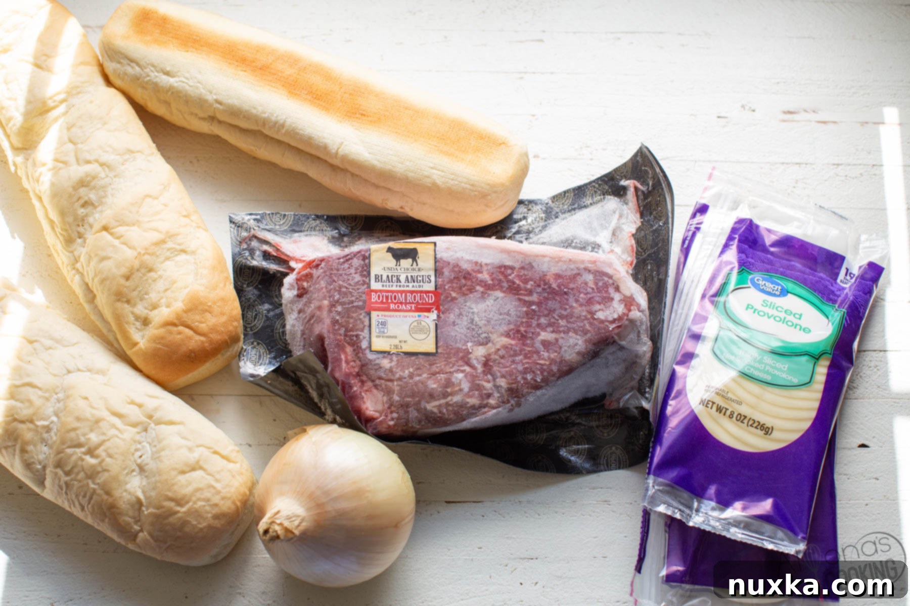 All the fresh ingredients needed to prepare a delicious homemade Philly Cheesesteak sandwich, including raw beef, onions, cheese slices, and long bread rolls.