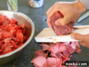 image of partially frozen beef being thinly sliced on a Mandoline slicer