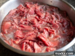image of marinated beef shavings in seasoning and a quick meat tenderizer for Philly Cheesesteak sandwiches