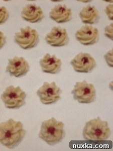 Raspberry jam being carefully piped into the center of unbaked flower cookies