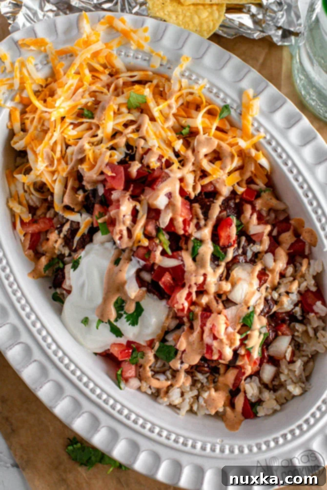 A beautifully layered homemade burrito bowl, featuring seasoned rice, black beans, vibrant salsa, creamy sauce, and fresh cilantro, served in an oval plate, ready to be enjoyed.