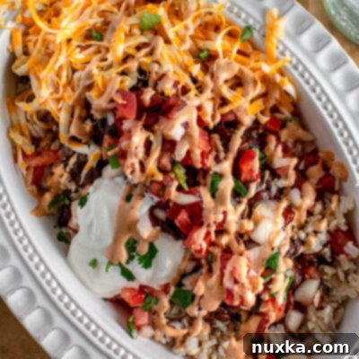 A vibrant and fresh homemade burrito bowl, featuring a base of seasoned rice, topped with black beans, diced tomatoes, cilantro, and a creamy sauce, ready for serving.