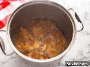 Deep-frying breaded chicken pieces in hot oil until golden brown and crispy for the homemade Popeyes chicken sandwich.