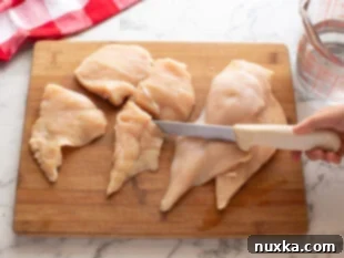Detailed view of cutting chicken breasts horizontally and pounding them to create bun-sized fillets for a Popeyes chicken sandwich.