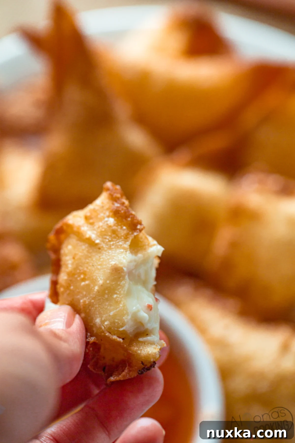 a bitten wonton shaped crab rangoon filled with cream cheese, sugar, and imitation crab meat dipped into duck sauce.