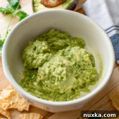 Close-up of a bowl of fresh, simple homemade guacamole with lime wedges and a spoon