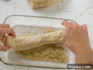Dredging shaped sub roll dough in Italian herb blend.