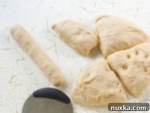 Subway bread dough being divided and shaped into logs on a floured surface.