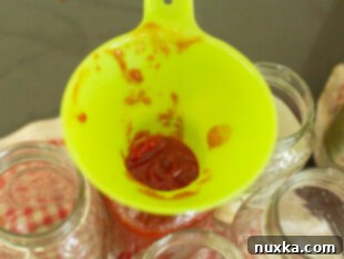 pouring tomato ketchup in a canning jar through a funnel