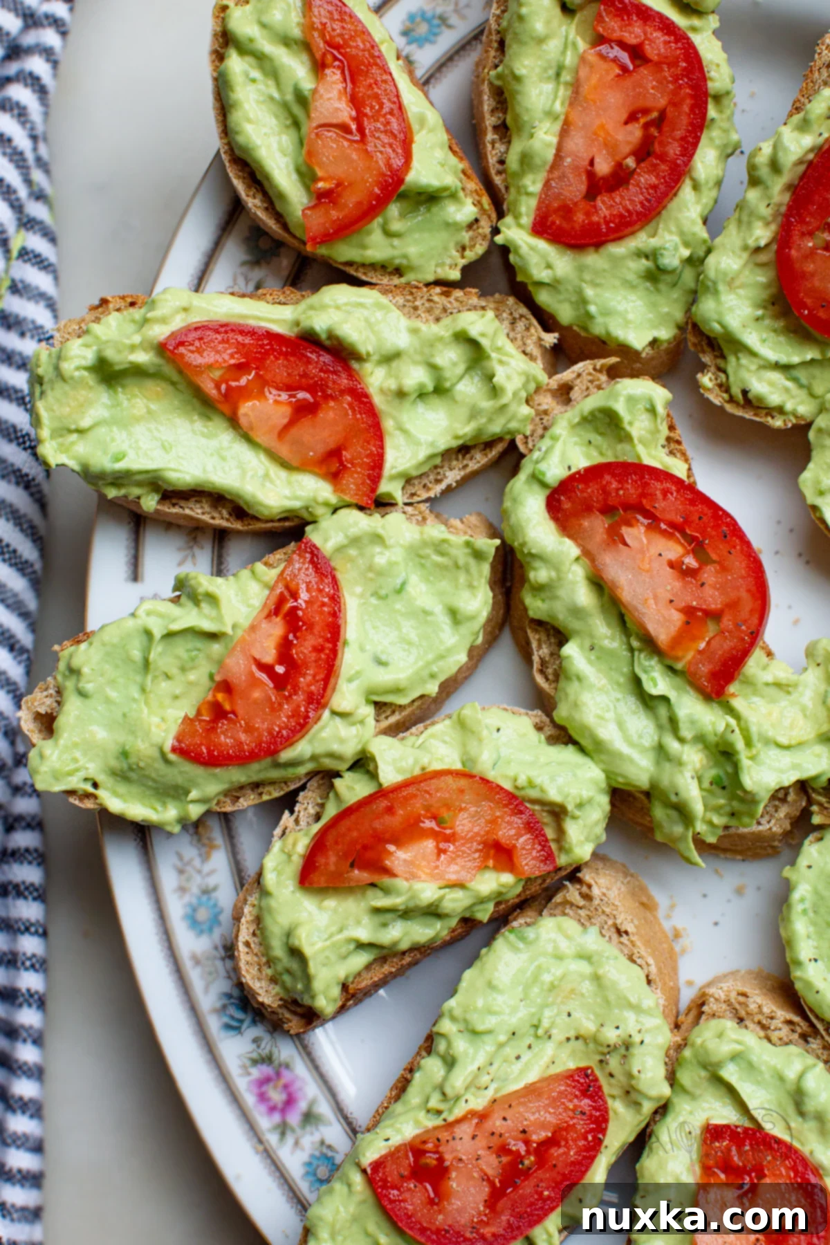 Delicious tomato avocado canapés with creamy garlic spread on bread slices, garnished with black pepper.