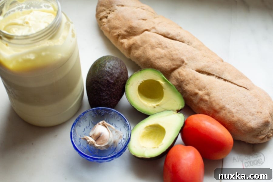 Fresh ingredients for creamy garlic avocado toast: baguette slices, ripe avocado, mayonnaise, garlic, and cherry tomatoes.