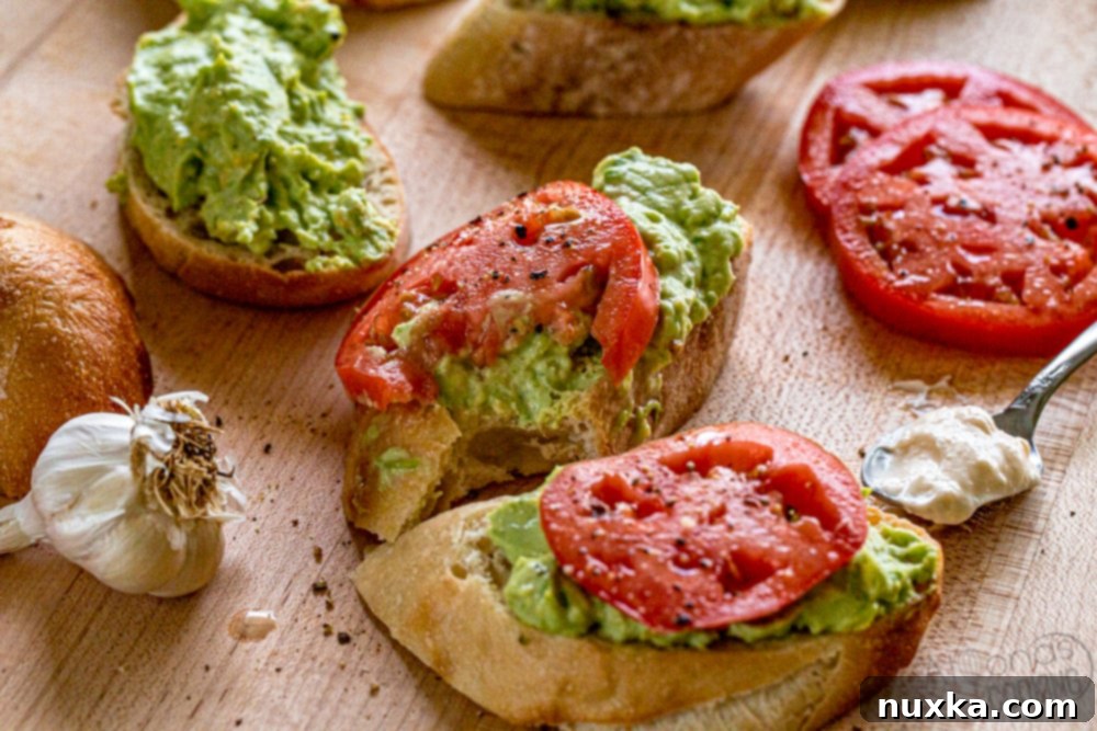 Avocado toast sandwiches with tomato, mayo, and garlic Assembled avocado toast sandwiches with tomato and garlic, beautifully presented on a wooden board.