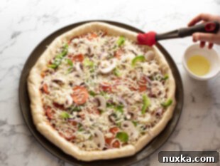 topping stuffed crust pizza with ingredients and brushing with oil