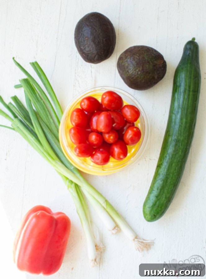 Ingredients for Avocado Salad: crisp cucumbers, grape tomatoes, soft avocados, green onions, sweet red bell pepper, avocado oil, white distilled vinegar, salt, and pepper laid out on a wooden board.