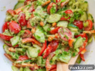 A finished cucumber tomato avocado salad in a large salad bowl, tossed with creamy dressing