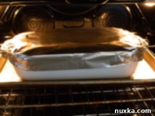 Baking a large, deep dish cream cheese lasagna, covered with foil, in the oven.