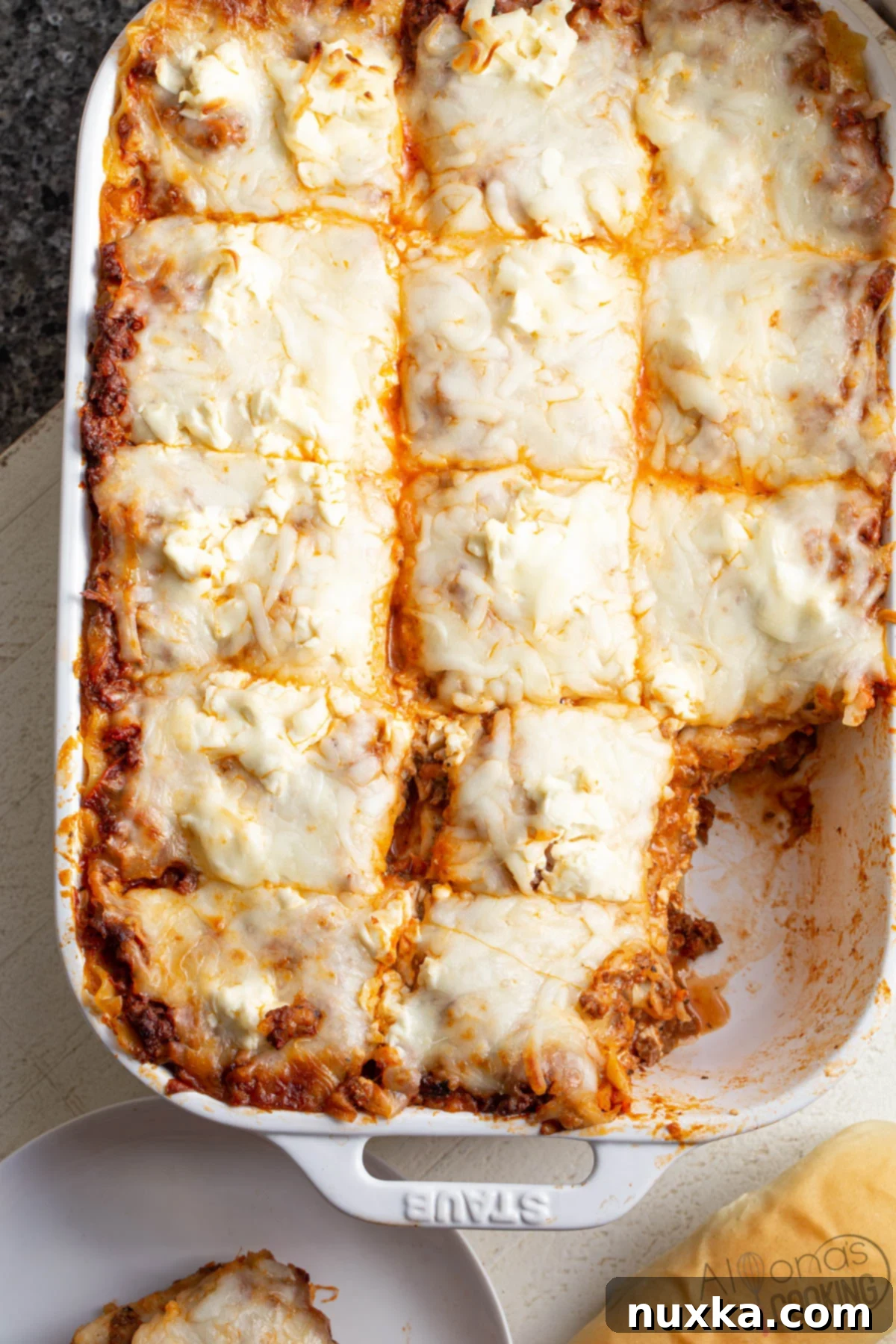 Cream cheese lasagna served with a slice of bread, showcasing layers of wide pasta noodles, rich Ragu meat sauce, generous cream cheese, and melted mozzarella, creating an incredibly creamy texture.
