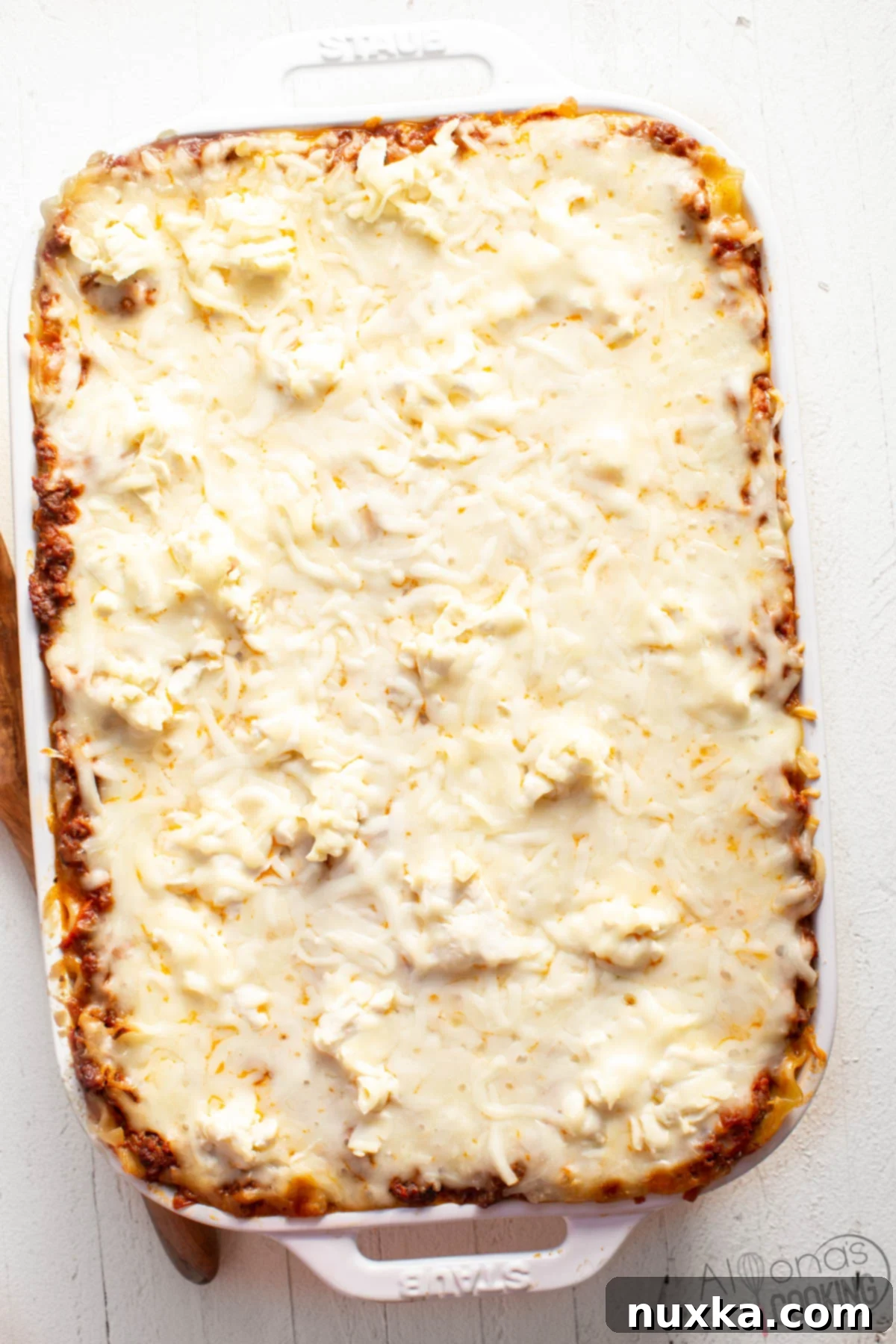 A whole, uncut lasagna casserole showcasing perfectly layered ruffle-edge noodles, rich meat sauce, melted cream cheese, and generous mozzarella cheese, all baked in a STAUB casserole dish.